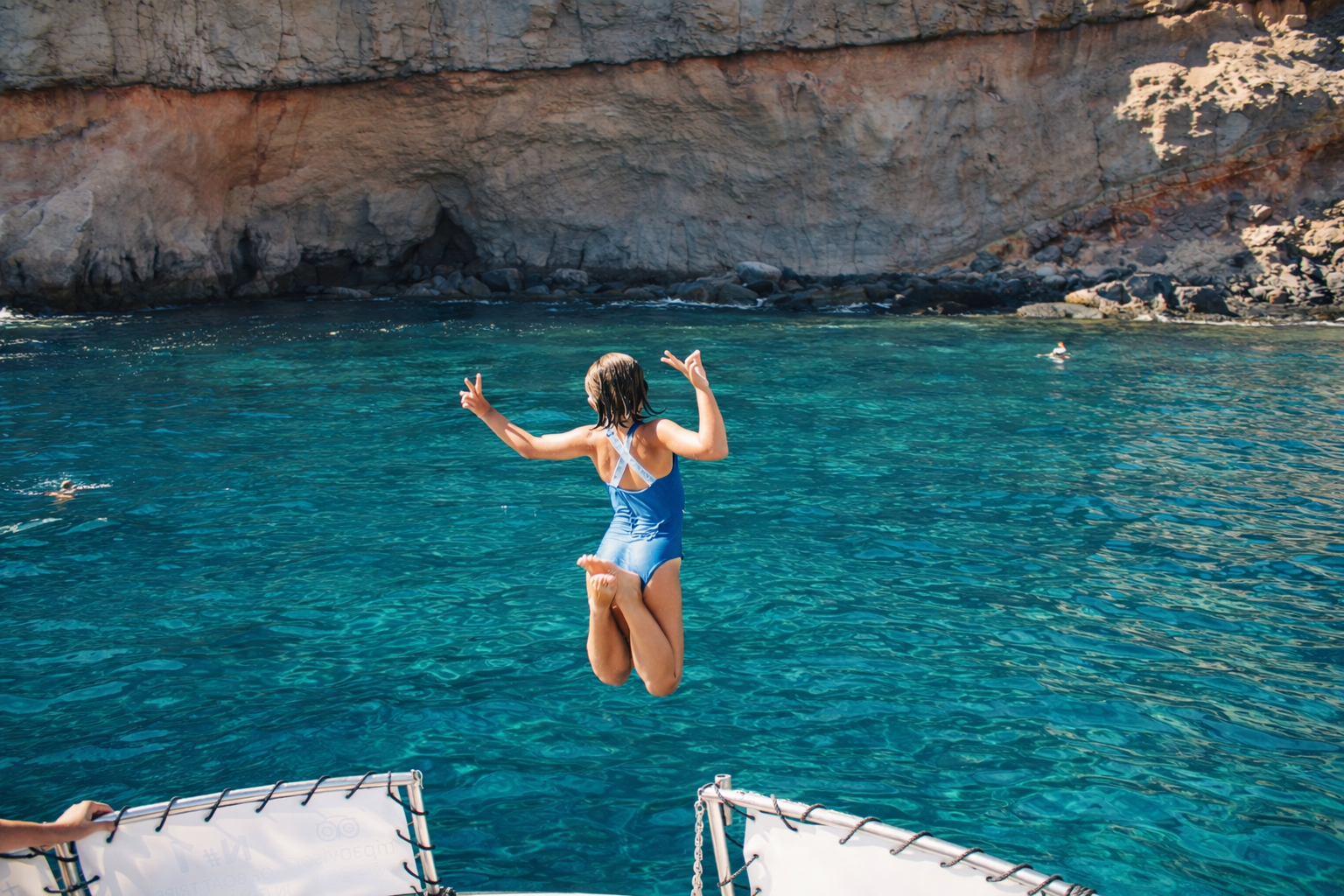Girl jumping into crystal clear turquoise water during a snorkeling boat trip in Puerto de Mogan, Gran Canaria