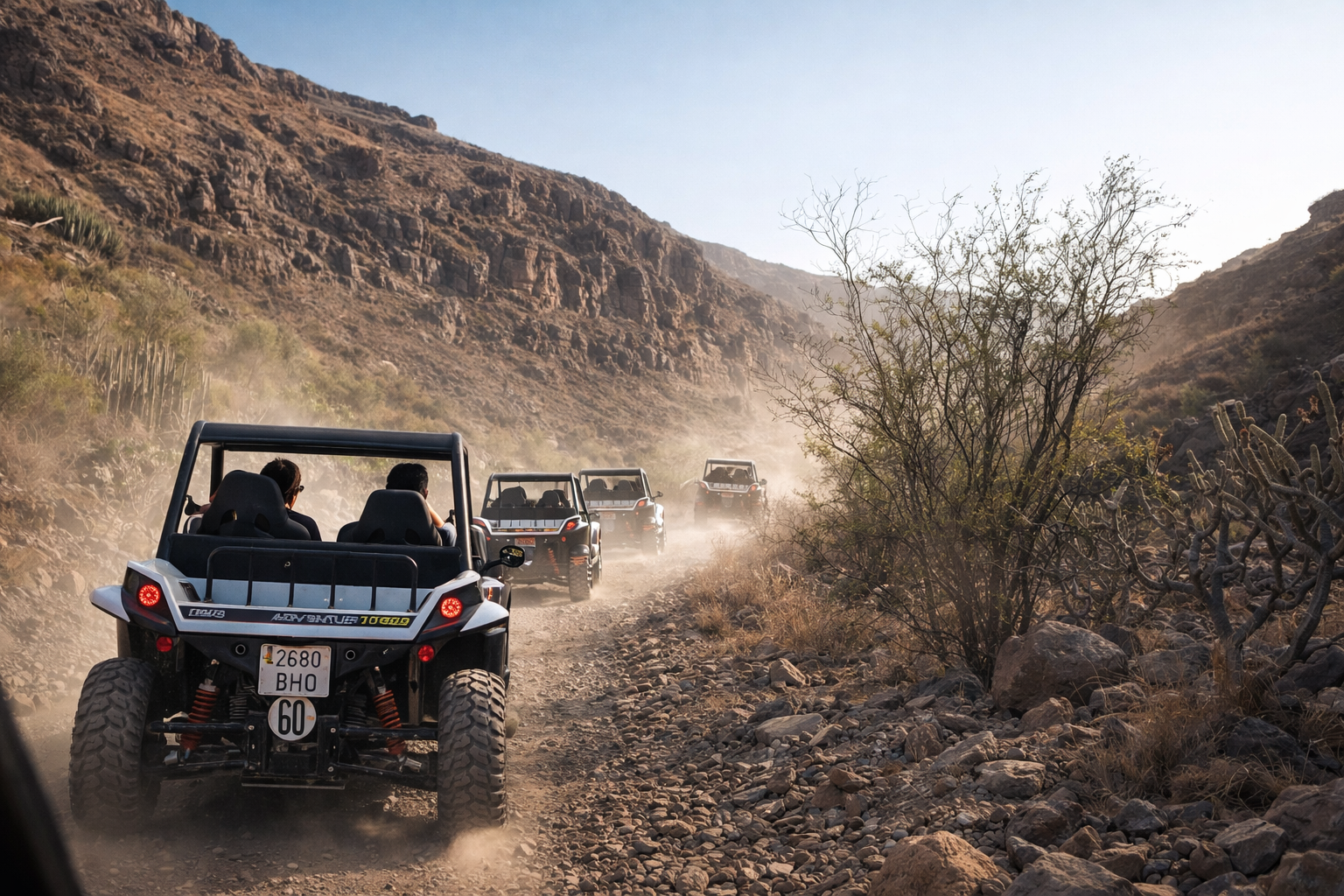 Off-road buggy tour driving through dusty mountain trails in Gran Canaria with scenic volcanic landscape and convoy of buggies
